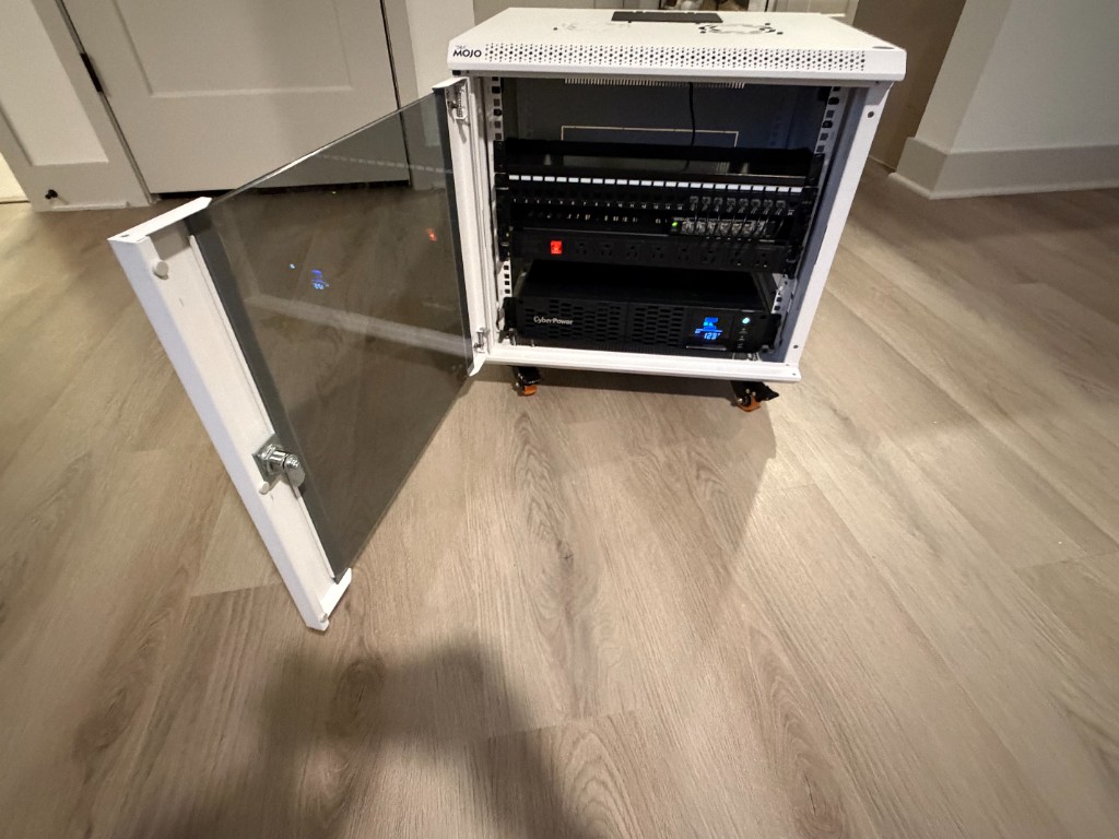 Front view of compact rack cabinet with glass door open, displaying patch panel, PDU, and CyberPower UPS.